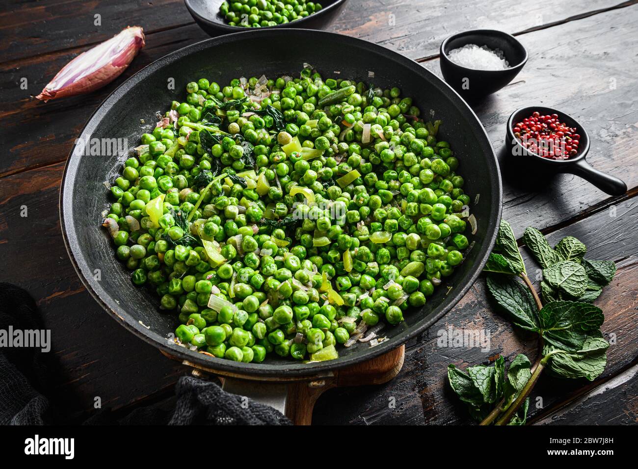 Piselli funghi ricetta senza glutine in padella e piselli in ciotola con pepe di scalogno di menta e vista laterale del sale sulla superficie di legno del vecchio pub primo piano nuovo largo A. Foto Stock