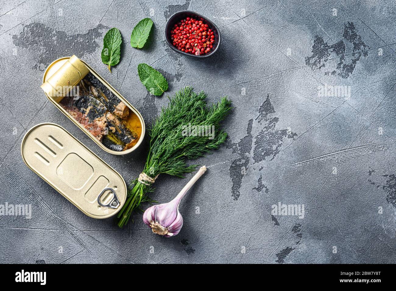 Sardinops in olio in conserva cibo in scatola, chiuso e aperto barattolo erbe di erbe di woth e aglio ocer grigio sfondo spazio di vista dall'alto per il testo. Foto Stock