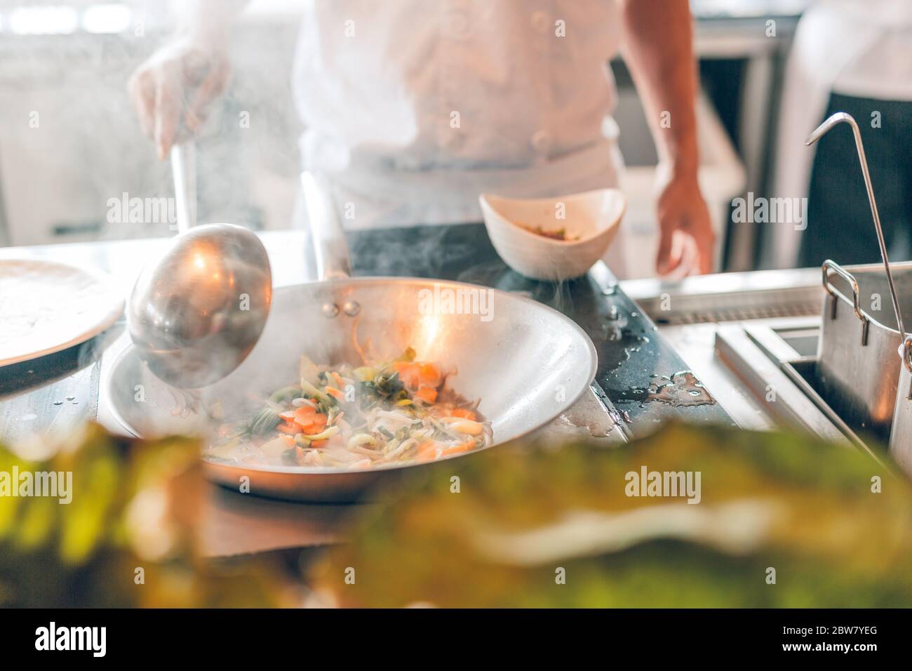 Primo piano di lavoro chef che prepara cibo cinese, cibo frittura in wok pain. Interni del ristorante asiatico. Foto Stock