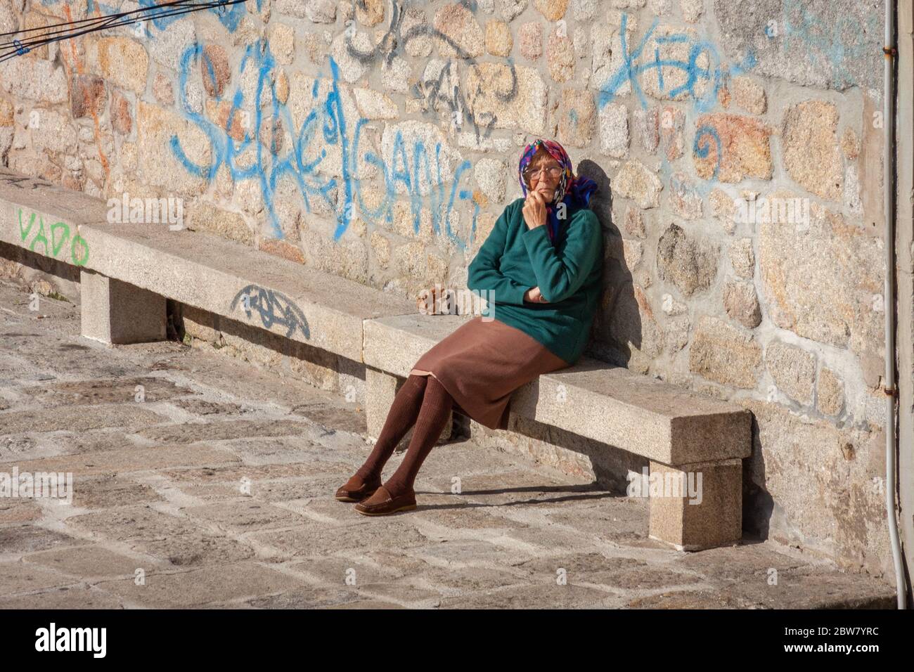 Una donna anziana seduta sulla panchina fuori casa a Porto, Portogallo Foto Stock