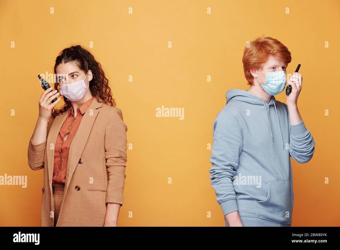 Due giovani agenti o addetti alla sicurezza che utilizzano walkie talkie mentre si levano in piedi a muro e segnalano qualsiasi tipo di violazione Foto Stock