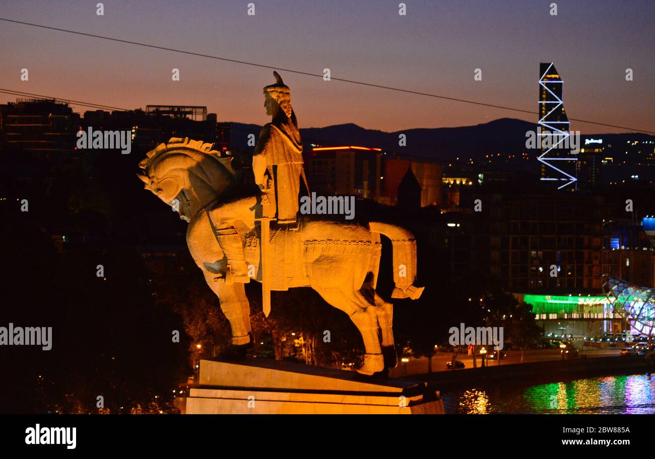 Tbilisi: Monumento del re Vakhtang Gorgasali, al crepuscolo, con il fiume Kura, Ponte della Pace e le montagne sullo sfondo. Georgia Foto Stock