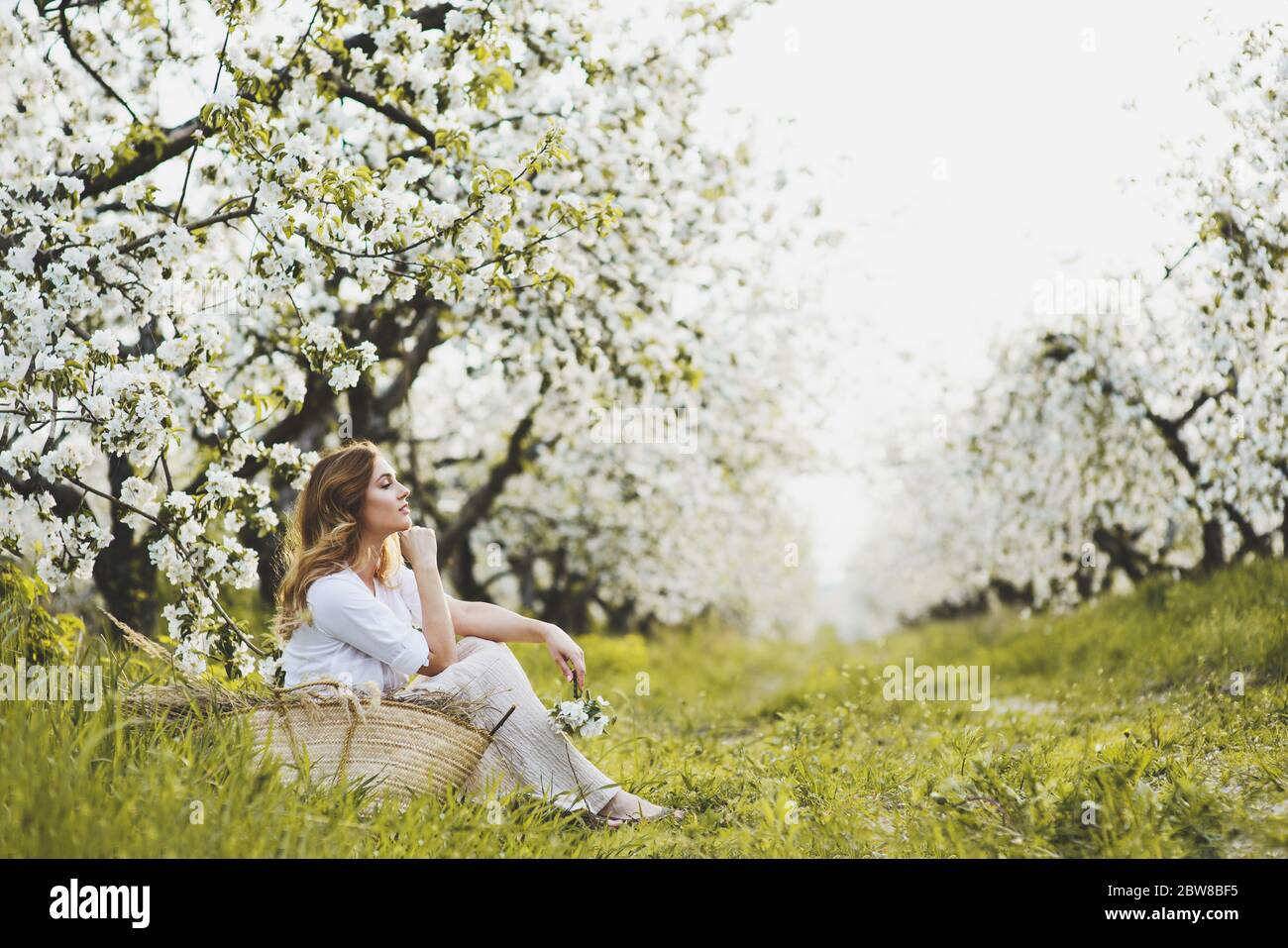 Bella donna romantica seduta sull'erba in giardino fiorito. Foto Stock