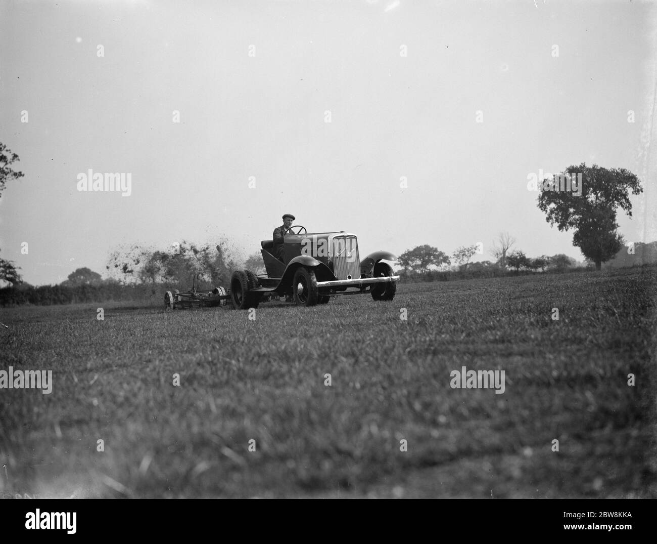 Falciatura dell'erba con il rasaerba agganciato alla parte posteriore di un camion o di un trattore da golf . 1937 Foto Stock