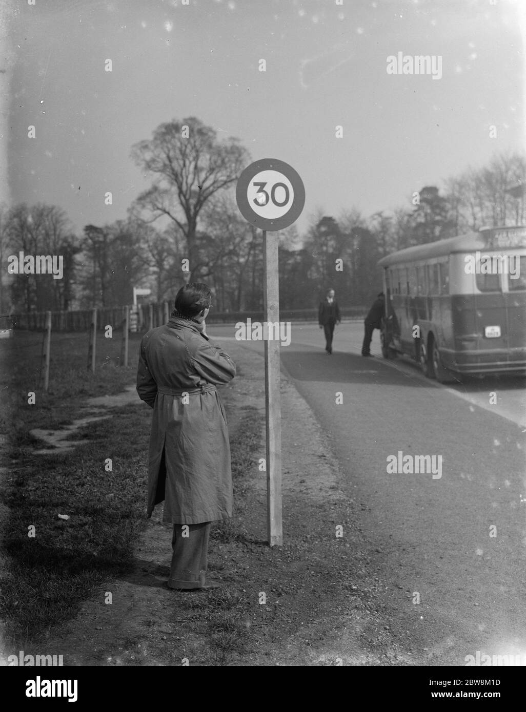 Un uomo che guarda il cartello stradale che indica il limite di velocità di 30 miglia all'ora . 1935 Foto Stock