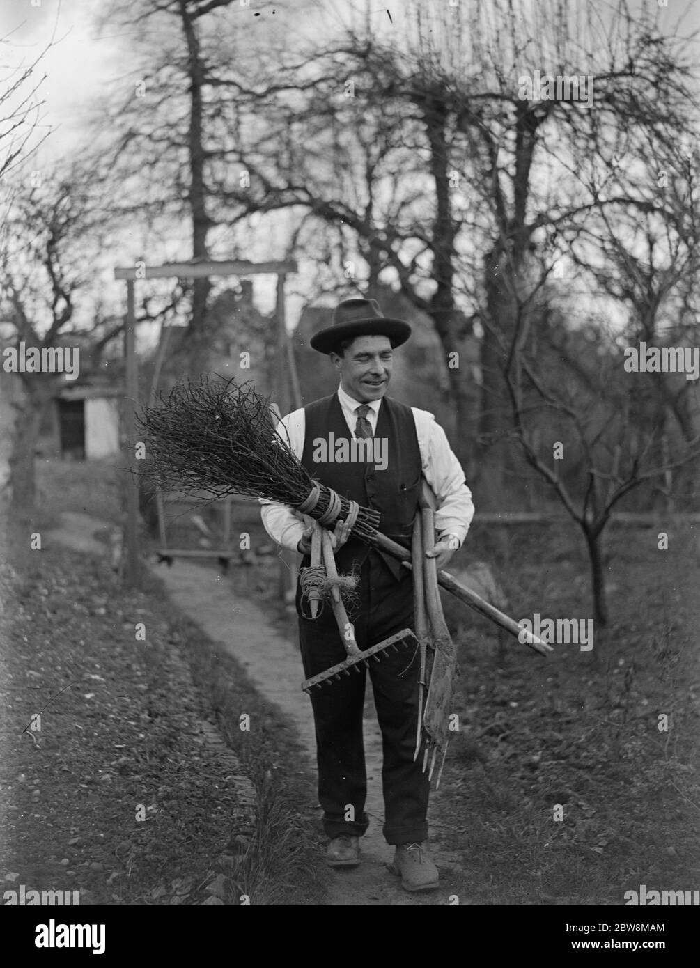 Uomo che porta attrezzi da giardino , rastrello , spade e scopa per besom . 1935 Foto Stock