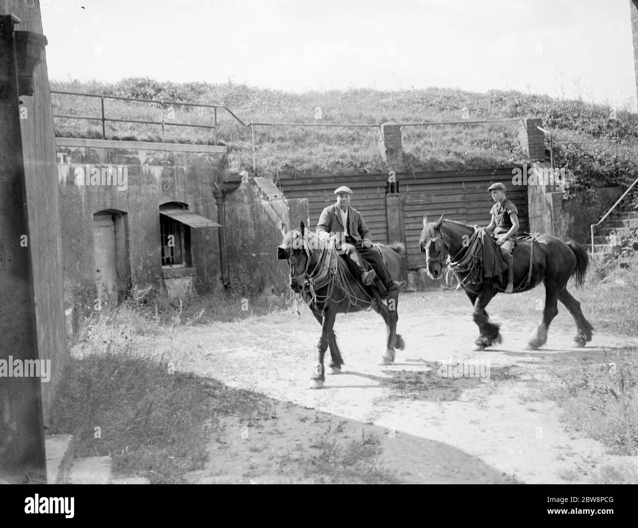 I lavoratori agricoli cavalcano i cavalli di lavoro passando un vecchio Fort sulla fattoria di Pedham Place a Farningham , Swanley, Kent, Inghilterra . 1935 Foto Stock