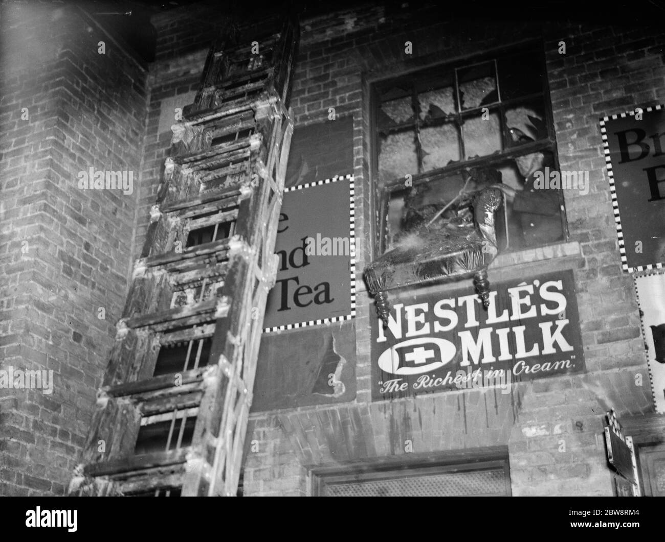 La brigata antincendio che si occupa di un incendio in un negozio di Foots Cray a Kent . Una scala fino alla finestra del primo piano e un pompiere che getta via i mobili bruciati . 13 dicembre 1935 Foto Stock