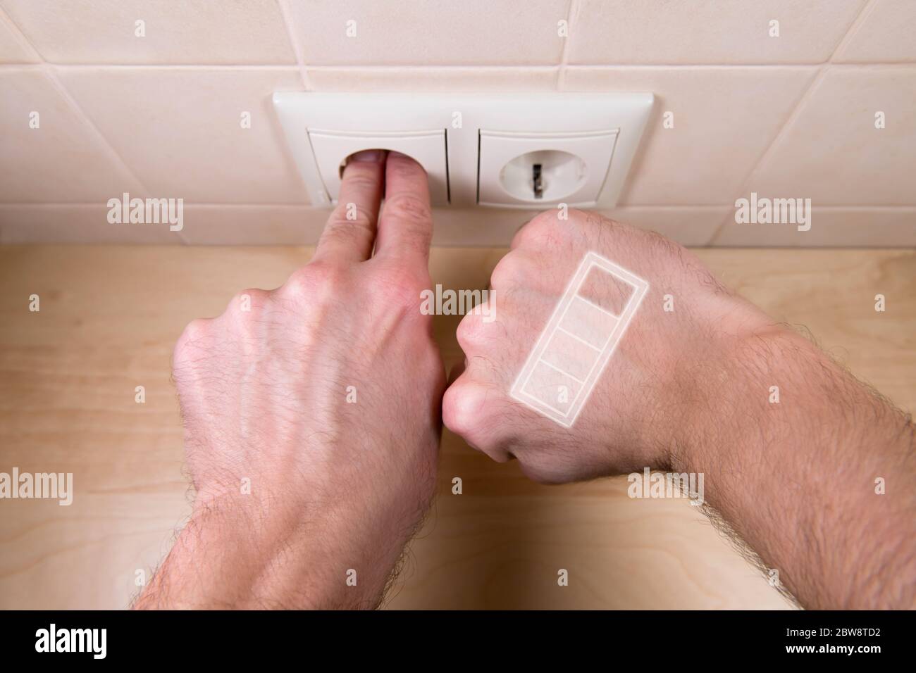 un uomo si sta caricando da una presa domestica inserendo le dita in essa. L'indicatore di carica è Foto Stock
