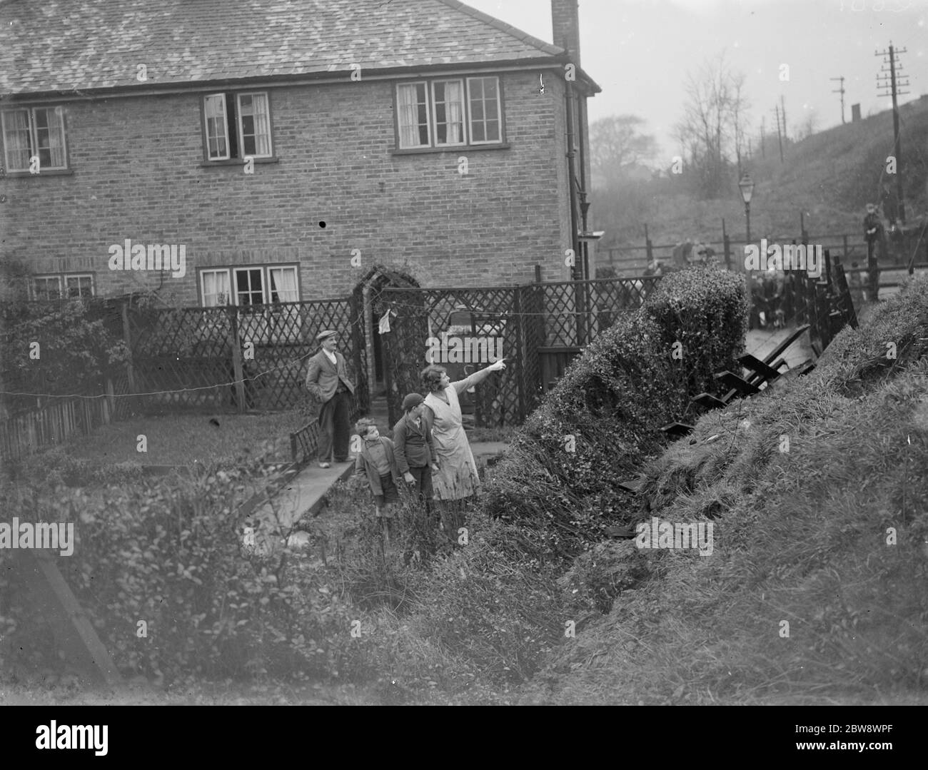 La gente guarda dai giardini posteriori mentre gli uomini lavorano per liberare lo scivolo della terra sulla linea ferroviaria di Wellhall . 1936 Foto Stock