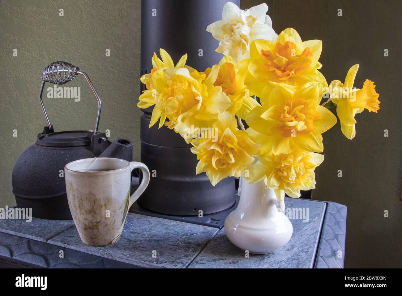 Bel bouquet di narcisi primaverili sulla stufa a legna con una tazza di tè caldo Foto Stock