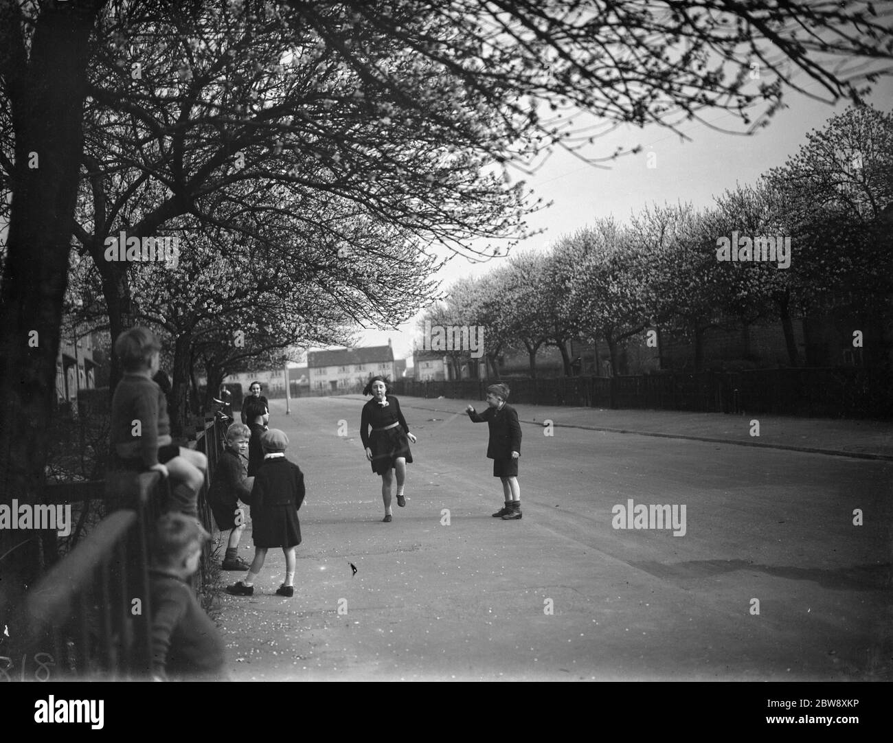 Bambini che giocano un gioco di salto sotto gli alberi di mandorle Blosson a Crayford . 1938 Foto Stock