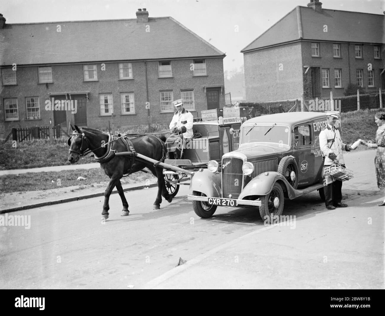 Un cavallo e un carrello di consegna espresso dei latticini sorpassa un van di Bedford di consegna espresso dei latticini. 1936 Foto Stock