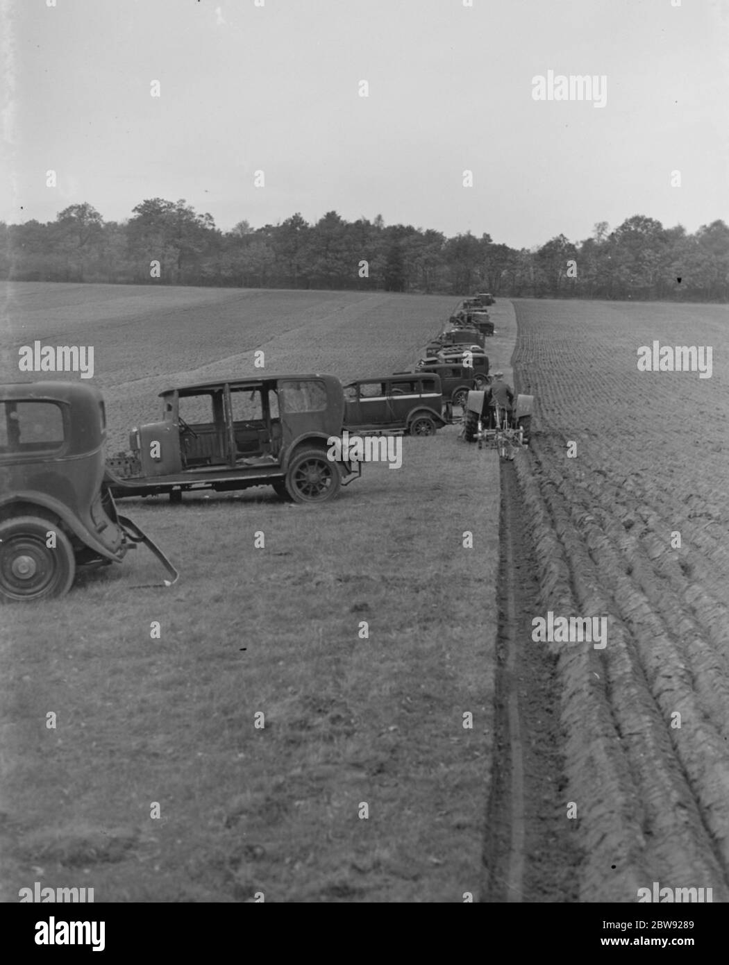 Un coltivatore che aratura un campo con un trattore . Accanto a queste si trovano vecchie auto che sono state parcheggiate per provocare l'ostruzione agli alianti nemici che trasportano truppe d'invasione che potrebbero voler atterrare sul campo . 1939 . Foto Stock
