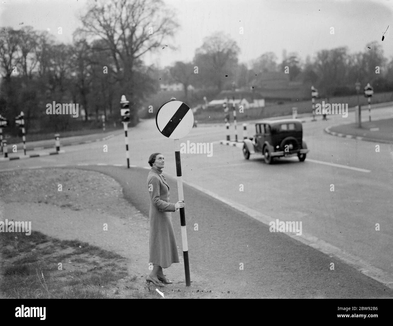 Una donna tiene un segnale di limite di velocità in corrispondenza di un incrocio stradale . 1938 Foto Stock