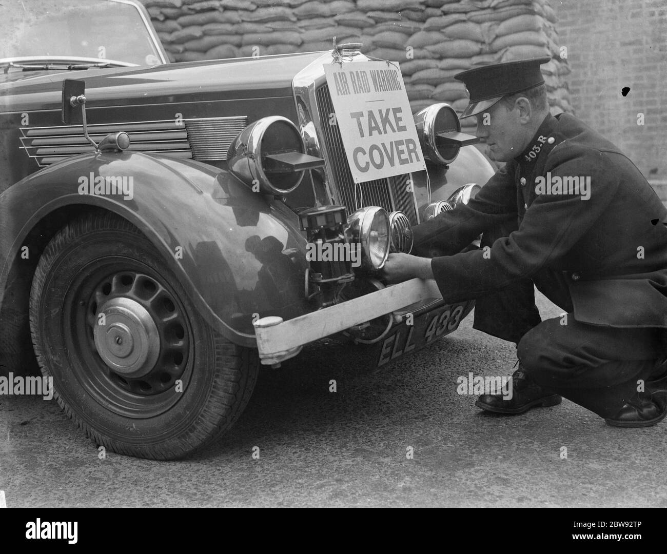 Un poliziotto sta montando una sirena RAID aria insieme ad un segnale di avvertimento ad un'automobile della polizia in Eltham, Kent . 1939 Foto Stock