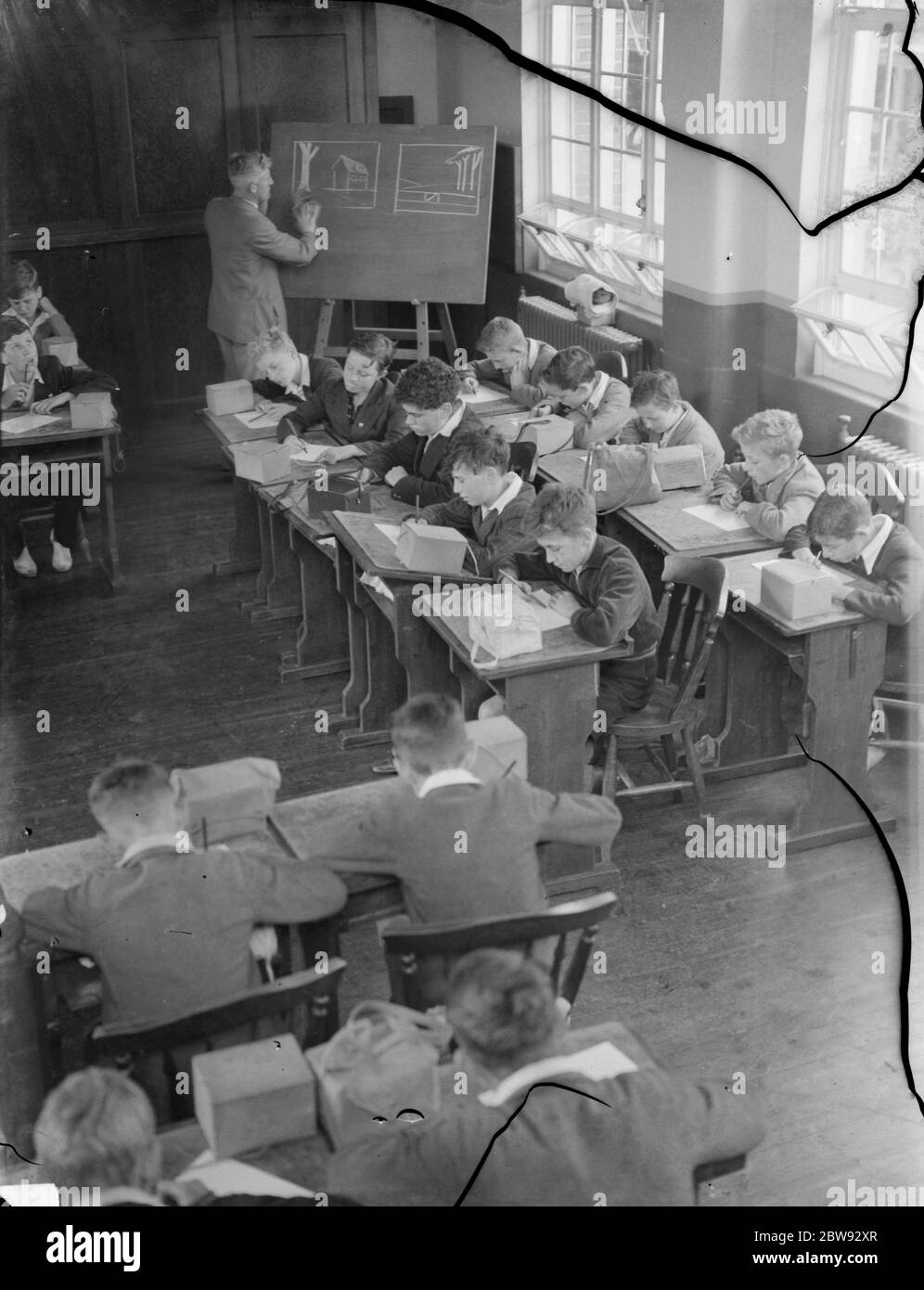 Bambini a scuola a Sidcup , Kent , durante la guerra . Qui sono in una lezione di disegno con le loro maschere a gas vicino a portata di mano in caso di bombardamento . 1939 Foto Stock
