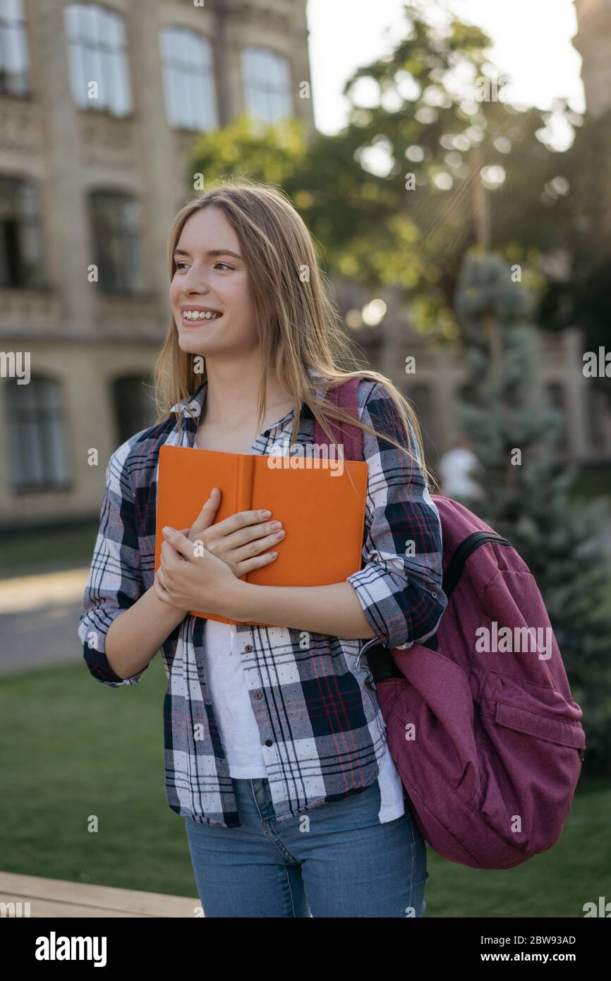 Ritratto di felice ragazza del college tenendo libro, in piedi nel parco. Studente di successo con zaino a piedi per l'università Foto Stock