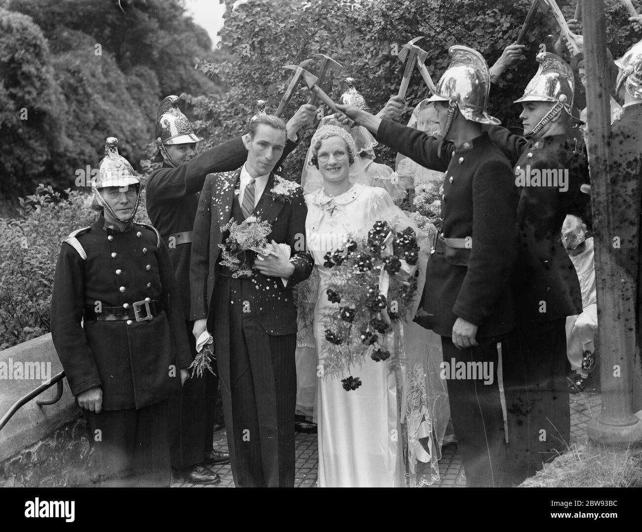 Il matrimonio dei vigili del fuoco di L Garland e di Miss C Magee . Lo sposo e lo sposo camminano attraverso l'arco di cazzi . 1939 Foto Stock