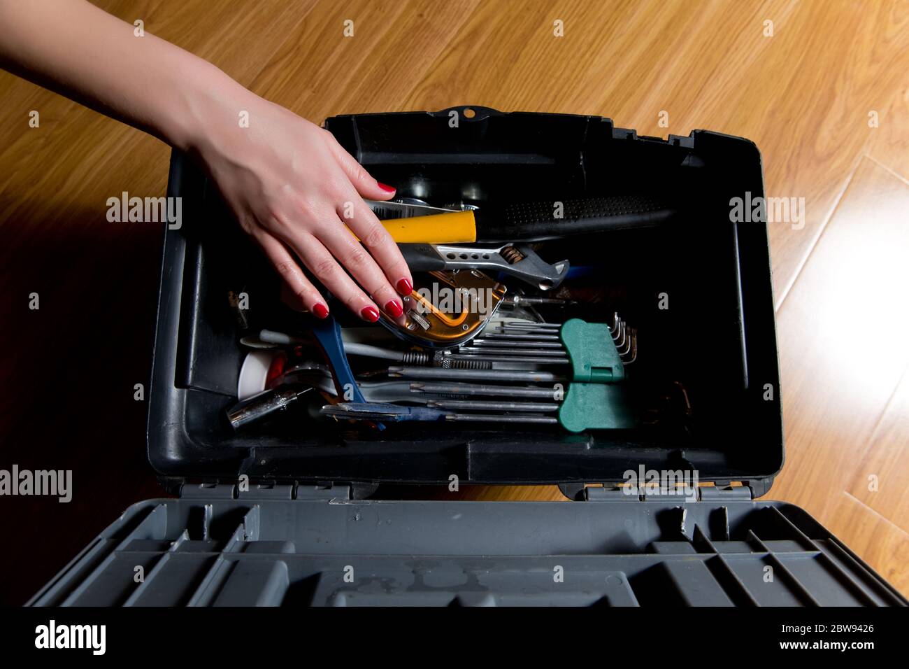 ragazza con manicure rossa raggiunge per gli attrezzi nella cassetta degli attrezzi. Lavoro femminile e maschile Foto Stock