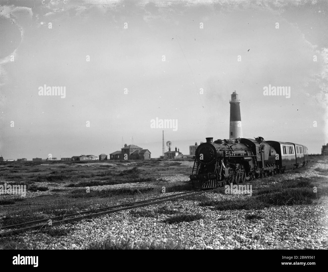 La ferrovia leggera Romney, Hythe & Dymchurch termina alla spiaggia di Dungeness. Questo motore sta lasciando la stazione , che si trova accanto al vecchio faro . La ferrovia Romney, Hythe & Dymchurch Railway è una ferrovia leggera di 381 in/15 mm di spessore nel Kent , Inghilterra . La linea di 131 km (22 miglia) collega le cinque porte di Hythe passando per Dymchurch , St. Mary's Bay , New Romney e Romney Sands fino a Dungeness . 1936 Foto Stock