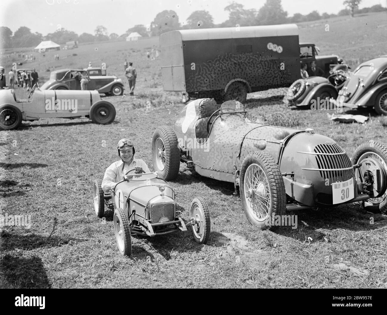 Peter McClure si siede in un'auto giocattolo da corsa , parcheggiata accanto alla cosa reale , a Lullingstone , Kent . 1936 . Foto Stock