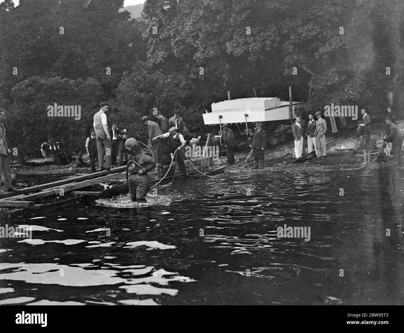 Prove record di velocità rimandate di nuovo quando Miss Inghilterra III fouls scivola . Kaye Don ha sostenuto un altro colpo di sfortuna nel suo tentativo di riconquistare il record mondiale di velocità dell'acqua per la Gran Bretagna in Miss Inghilterra III , Lord Wakefield ' s £ 40 , 000 velocità barca , a Loch Lomond , Scozia , quando lo scivolo che porta al bordo dell' acqua crollò e si strinse un buco nello scafo della barca . I subacquei dell'Ammiralty hanno lavorato tutta la notte per sostituire lo scivolo e fare un esame subacqueo del lavoro . Operai che portano una nuova rotaia giù alla riva per sostituire quella rotta mentre un subacqueo si alza vicino pronto per arrivare a. Foto Stock