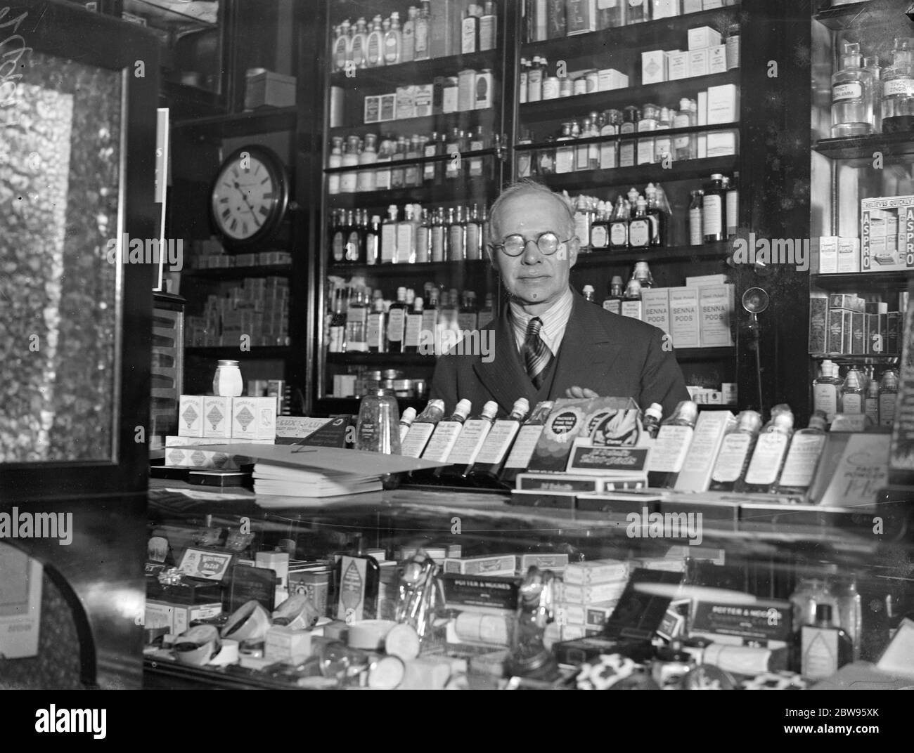 Negoziante legato da banditi a Londra . George Rackham , assistente di un negozio di farmacia a Charing Cross Road , Londra , fu attaccato da banditi che lo persero con i dusters e le corde e lo derubarono , prendendo denaro nella cassa del negozio , e scappato in auto . Il sig. George Rackham, dietro il banco del negozio in cui è stato attaccato da banditi. 6 maggio 1932 Foto Stock