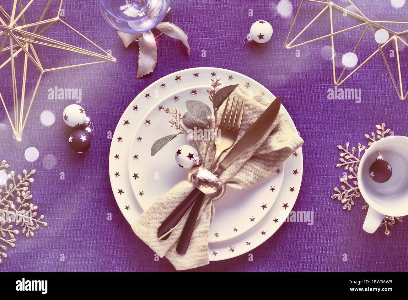 Tavolo natalizio con piatto bianco e utensili dorati e decorazioni dorate. Disposizione piatta, vista dall'alto su sfondo in tessuto di lino blu scuro. Xmas ligh Foto Stock