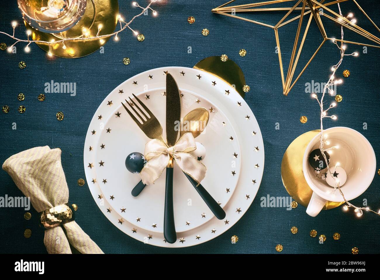 Tavolo natalizio con piatto bianco, utensili dorati e decorazioni dorate. Disposizione piatta, vista dall'alto sul retro in tessuto da tavolo di lino azzurro, verde scuro Foto Stock