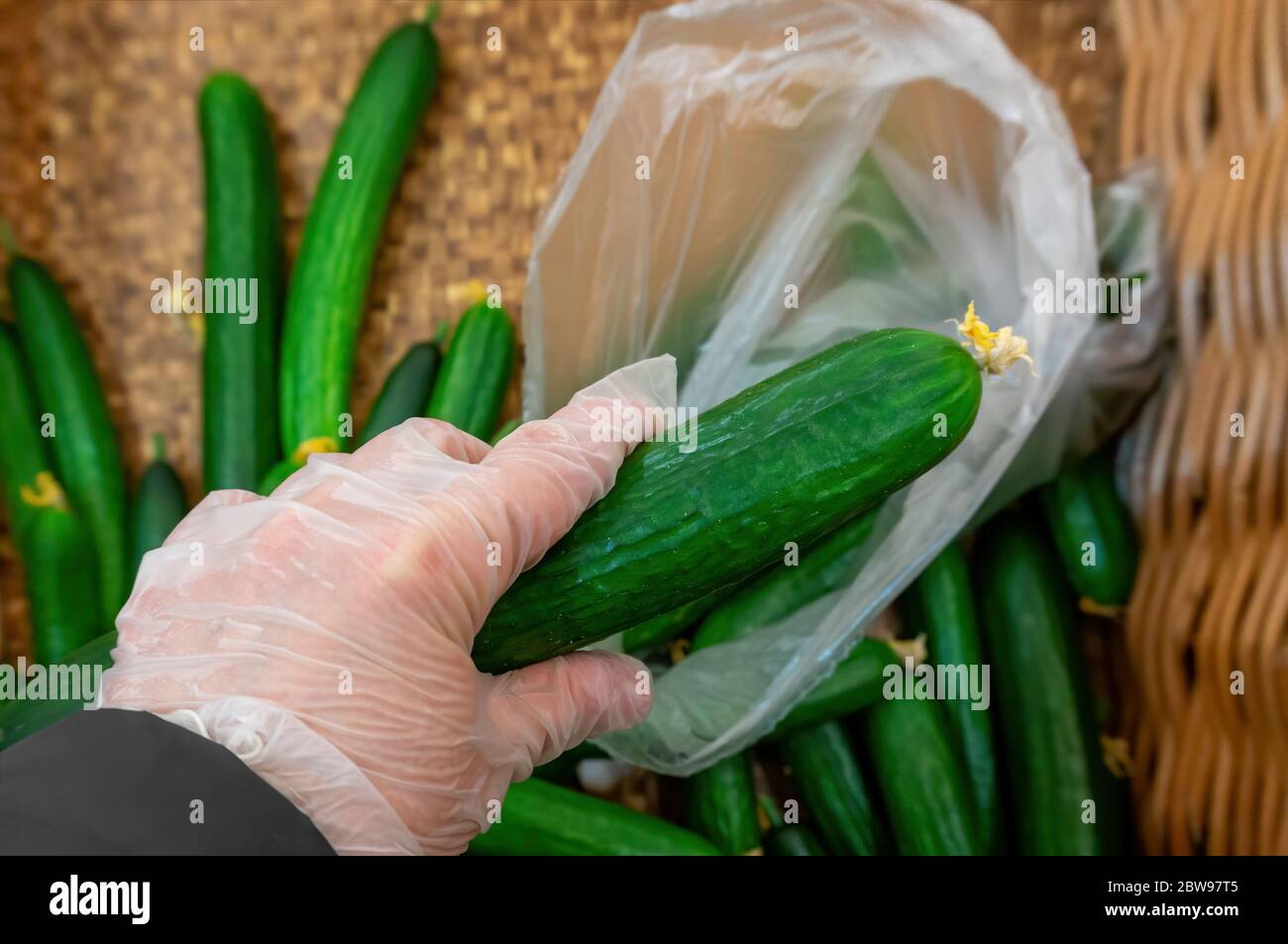 un acquirente di guanti mette i cetrioli in una borsa di plastica Foto Stock