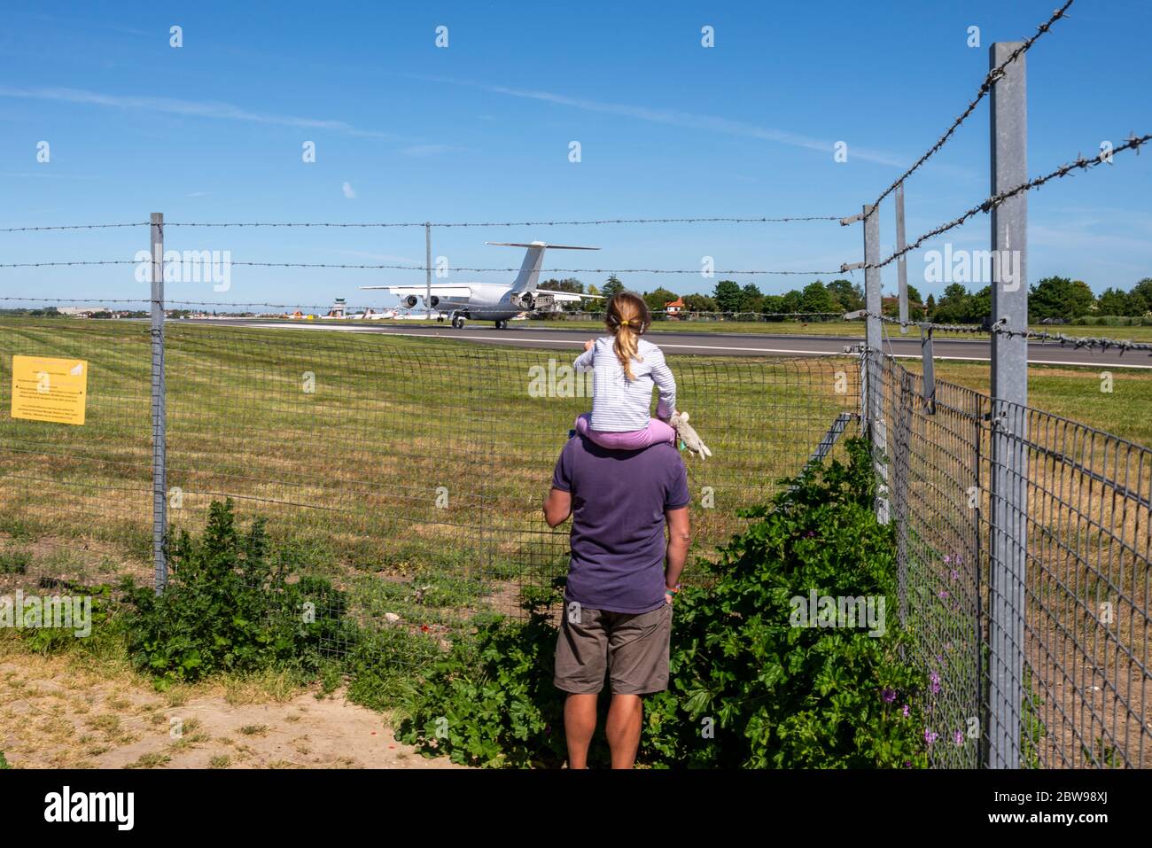 Padre e figlia che guardano un aereo atterra all'aeroporto di Southend, Essex, Regno Unito. Iniziare giovani. L'aereo ha individuato la recinzione dell'aeroporto Foto Stock
