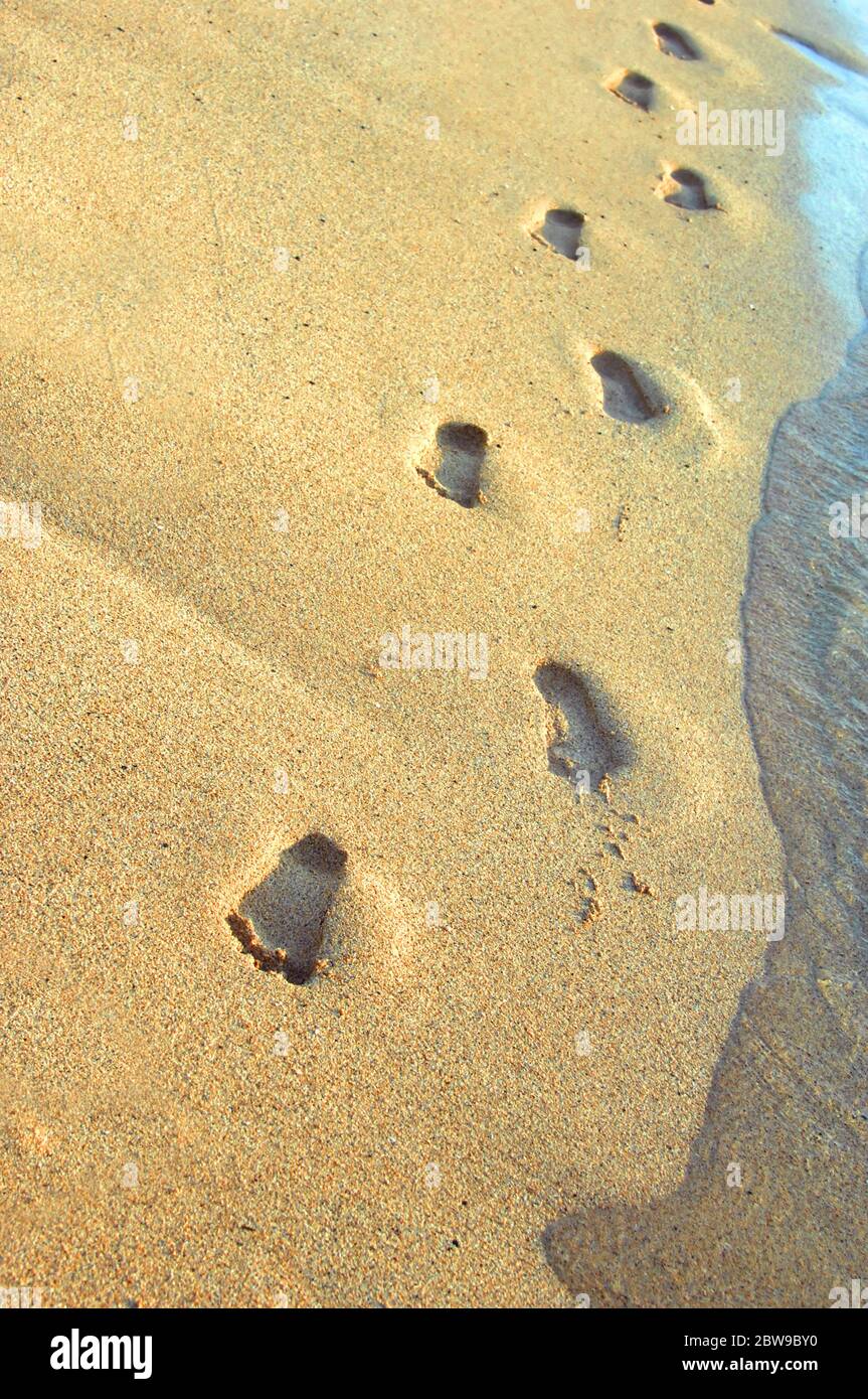 Le impronte nella sabbia mostrano i progressi verso la fotocamera. L'oceano si lava verso i passi. Foto Stock