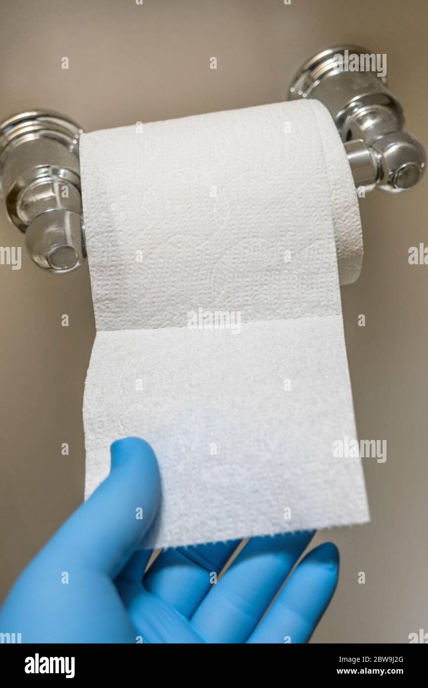 Primo piano della mano nel guanto in lattice blu che raggiunge la toilette carta Foto Stock