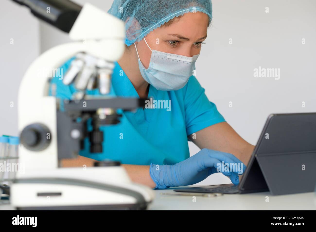 Tecnico di laboratorio che utilizza la tavoletta accanto al microscopio Foto Stock