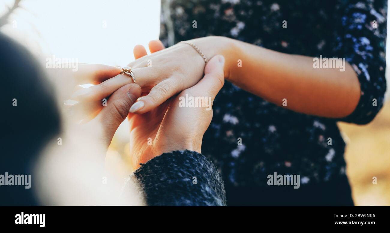 Uomo caucasico in ginocchio chiedendo il matrimonio la sua ragazza mentre si mette sul dito l'anello di nozze Foto Stock