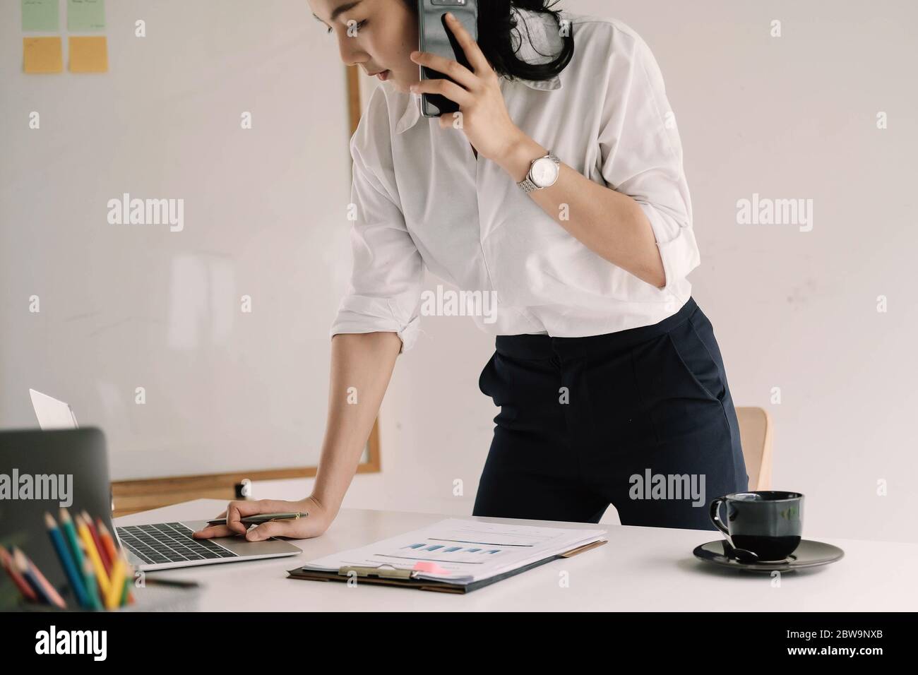 Giovane imprenditore femminile che lavora computer portatile e che parla telefono cellulare con il cliente Foto Stock