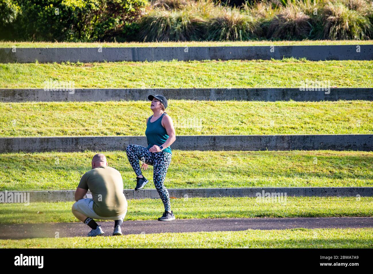 Donna che si esercita in lycra nel parco con personal trainer che guarda su, Sydney, Australia, esercizio di prima mattina Foto Stock