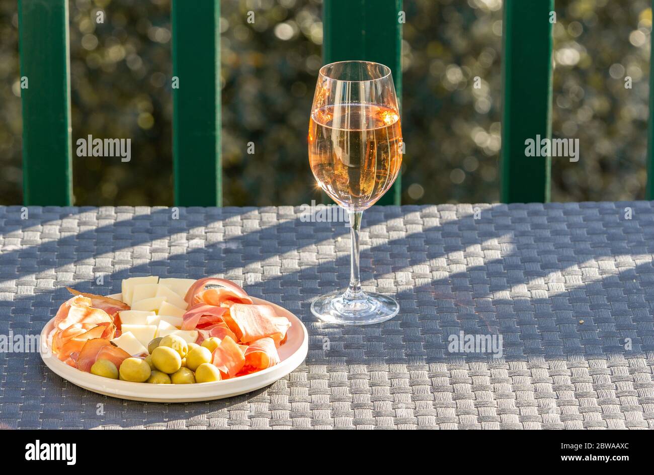 Bicchiere di rosone e piatto con prosciutto, prosciutto, olive, formaggio sulla tavola esterna. Spazio di copia. Foto Stock