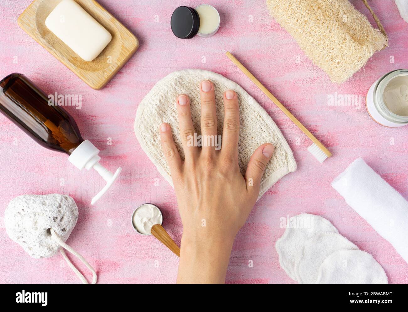 Accessori per bagno zero rifiuti sapone, spazzolino da denti, dentifricio, burro di karité, panno per lavaggi in loofah, contenitore in vetro riutilizzabile. Mano femminile sulla parte superiore. Vista dall'alto, layout. Foto Stock