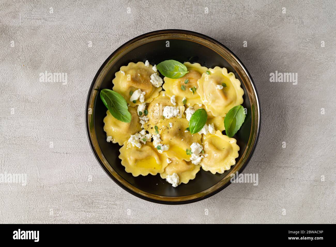 Pasta girasoli con formaggio morbido, olio d'oliva e foglie di basilico in ciotola nera isolata su fondo grigio. Pranzo o cena italiano, mediterraneo. Vista dall'alto. Foto Stock