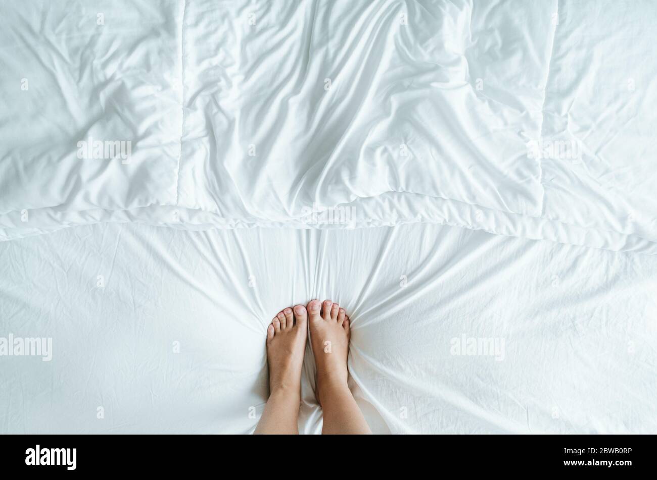 Piedi e piedi simmetricamente passo sui fogli bianchi rugosi del letto. Foto Stock