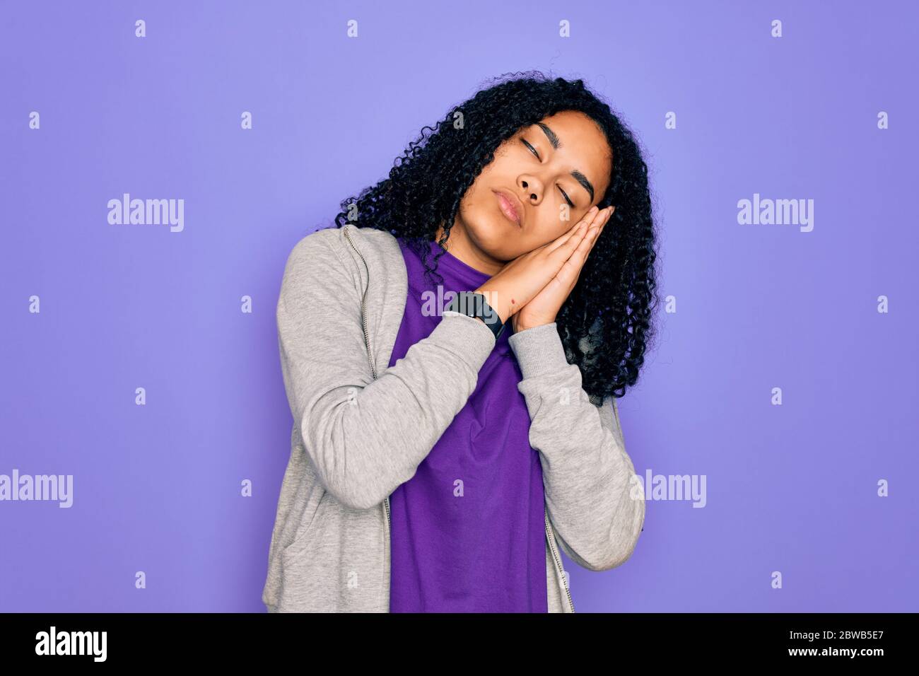 Giovane donna sportiva afroamericana con felpa casual su sfondo viola che dorme stanco sognando e posando con le mani insieme mentre puzzano Foto Stock