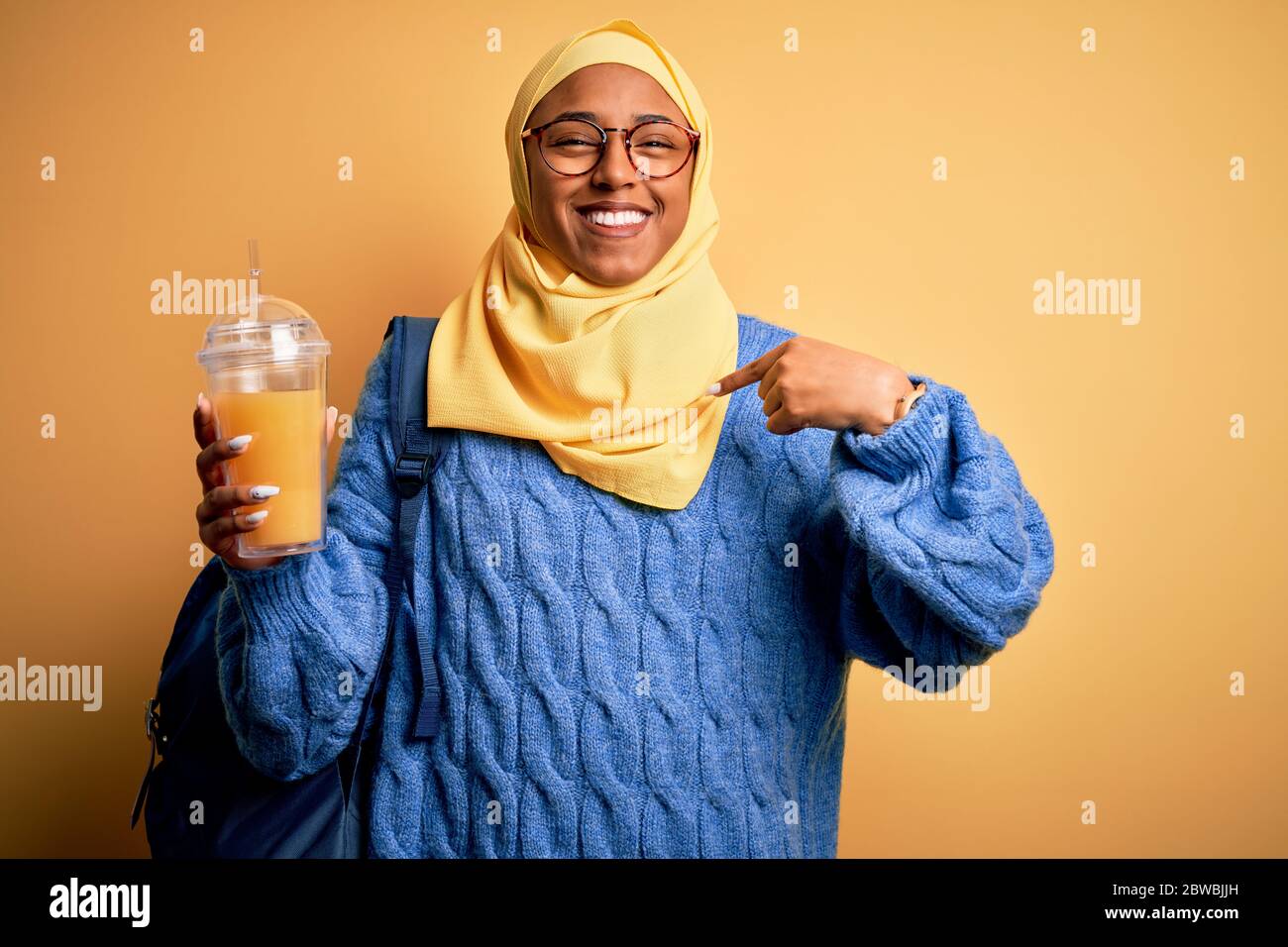 Giovane afroamericana afroturistica donna con hijab musulmano bere succo d'arancia con faccia a sorpresa che punta il dito verso se stesso Foto Stock