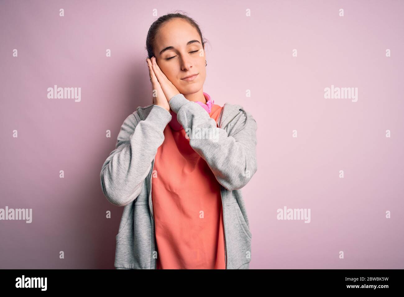 Bella donna sportiva che fa sport ascoltare musica con le cuffie su sfondo rosa dormire stanchi sognare e posare con le mani insieme WI Foto Stock