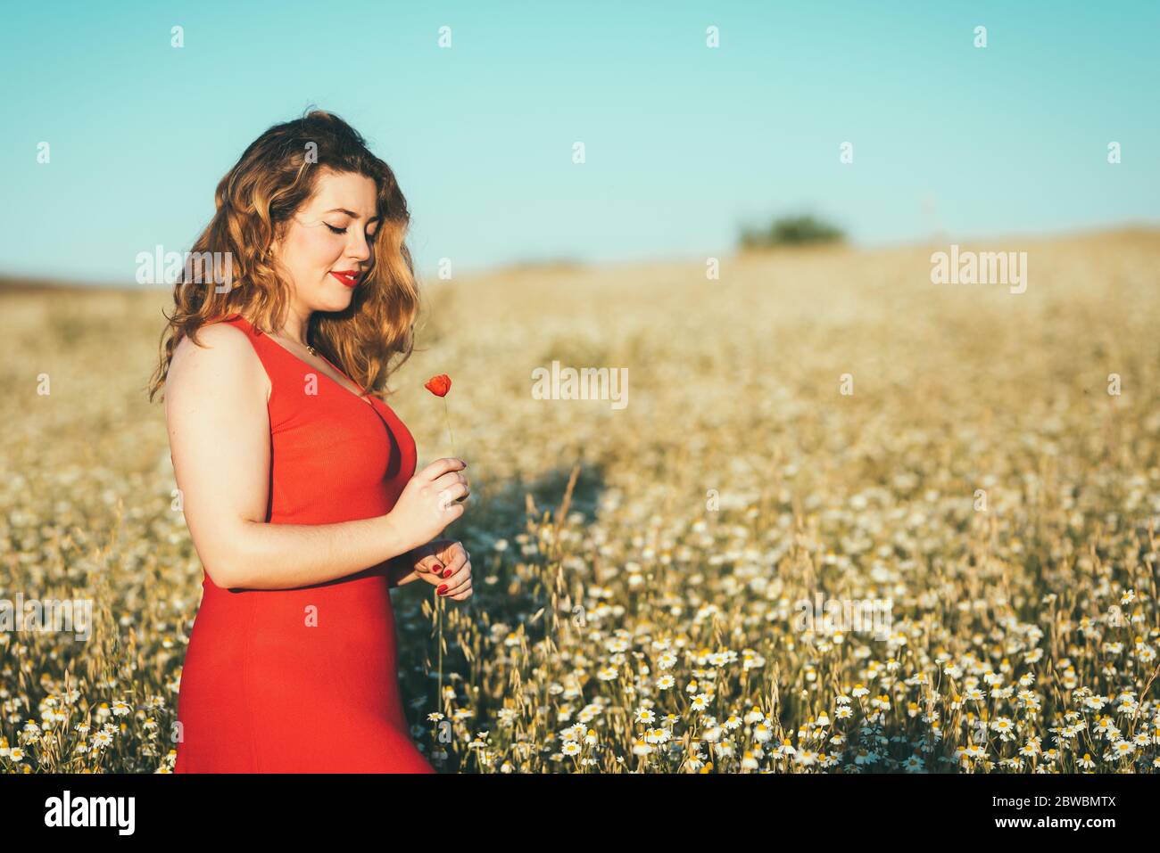 donna con abito rosso e papavero in mano nel campo. Foto Stock