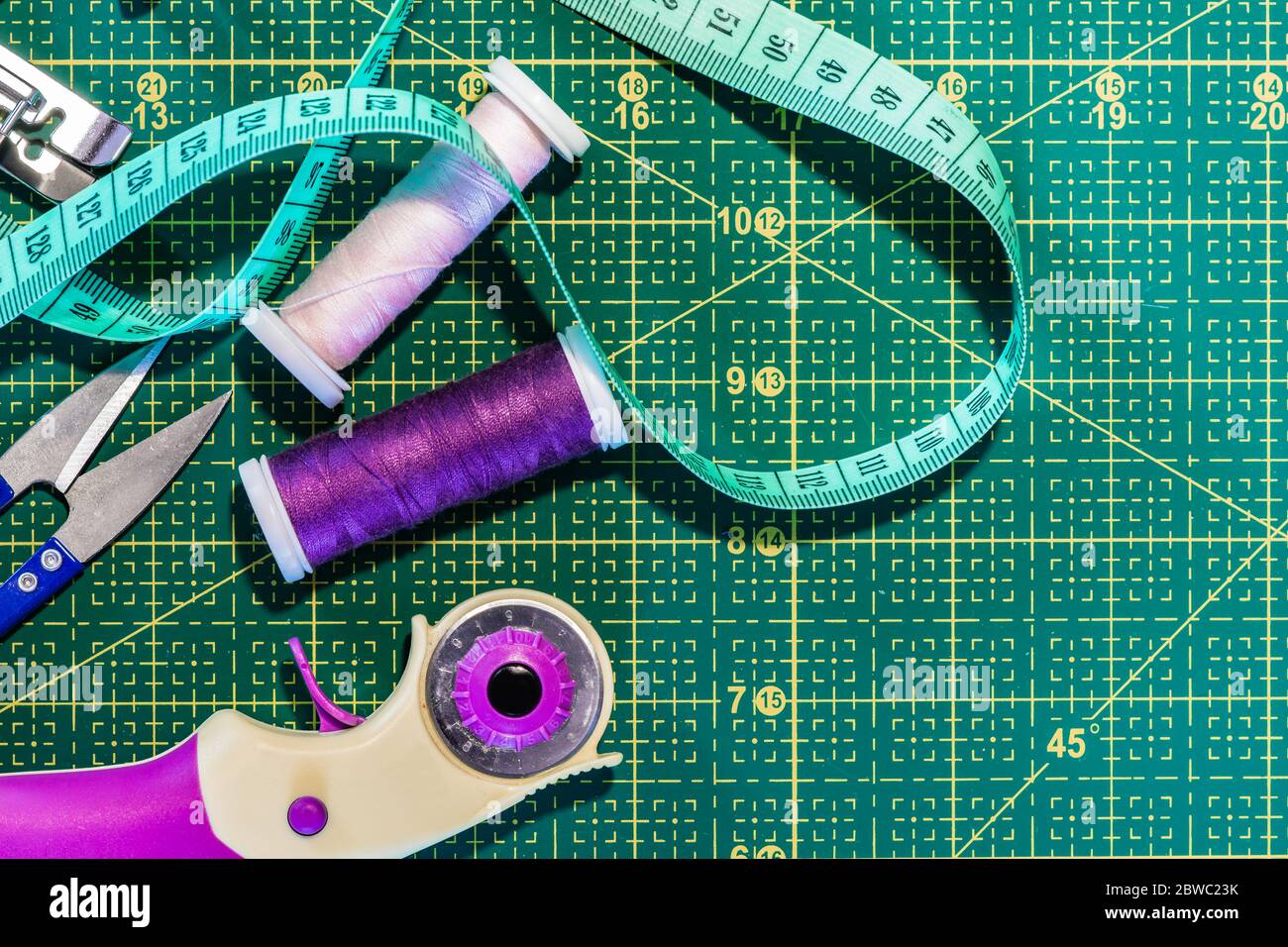 Cucitura piatto posare. Vista dall'alto degli accessori per cucire sul tappetino da taglio: Centimetri, perni e fili da cucire. Industria di dressmaaking Foto Stock