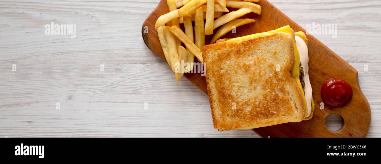 Hamburger di formaggio fresco alla griglia con fritte su un rustico asse di legno su uno sfondo di legno bianco, vista dall'alto. Posato piano, sopra, dall'alto. Spazio f Foto Stock