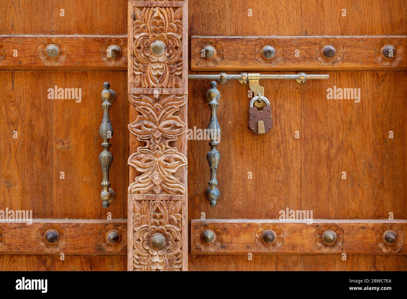 Particolare di porta in legno marrone con intagli e maniglie metalliche nel centro storico di al Mudairb in Oman Foto Stock