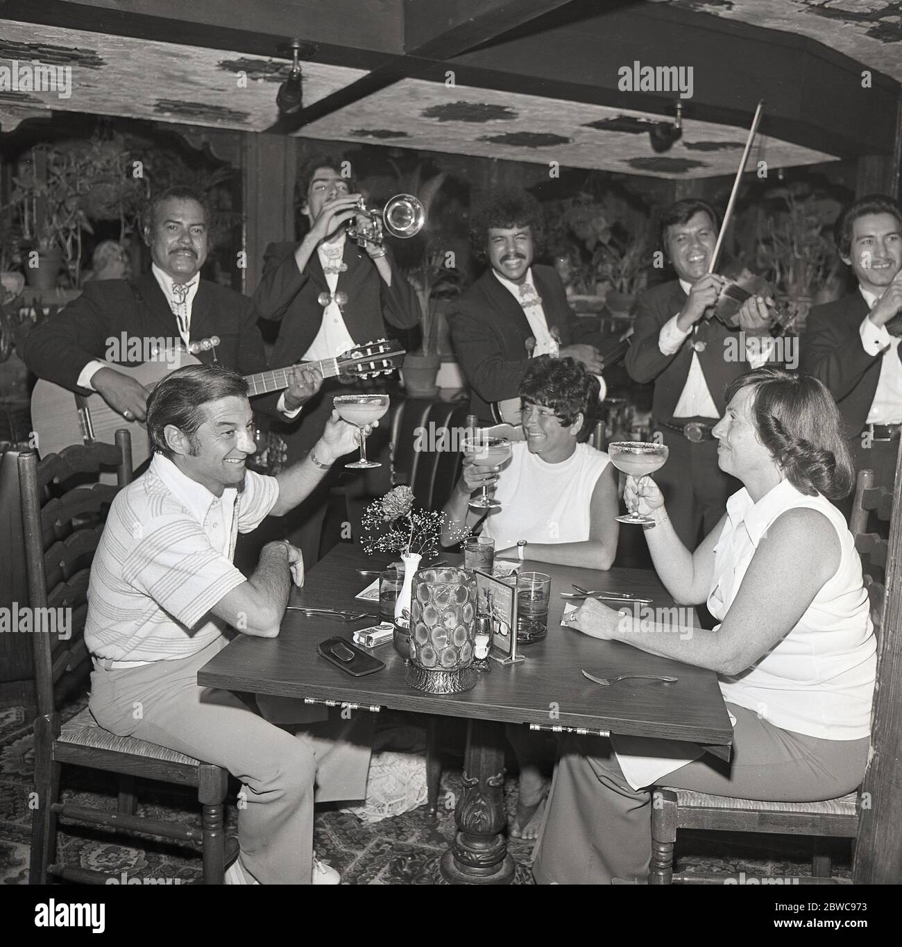 Anni '60, Historical, USA, California, Los Angeles, una band di tutti i maschi che suona musica per una e due donne che festeggiano con cocktail a un tavolo in un ristorante spagnolo. Foto Stock